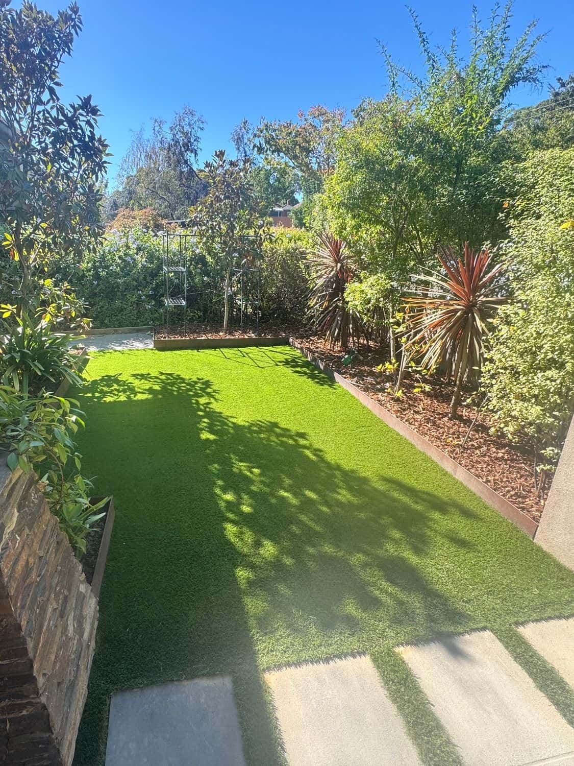 Artificial grass between concrete pavers and lush garden beds