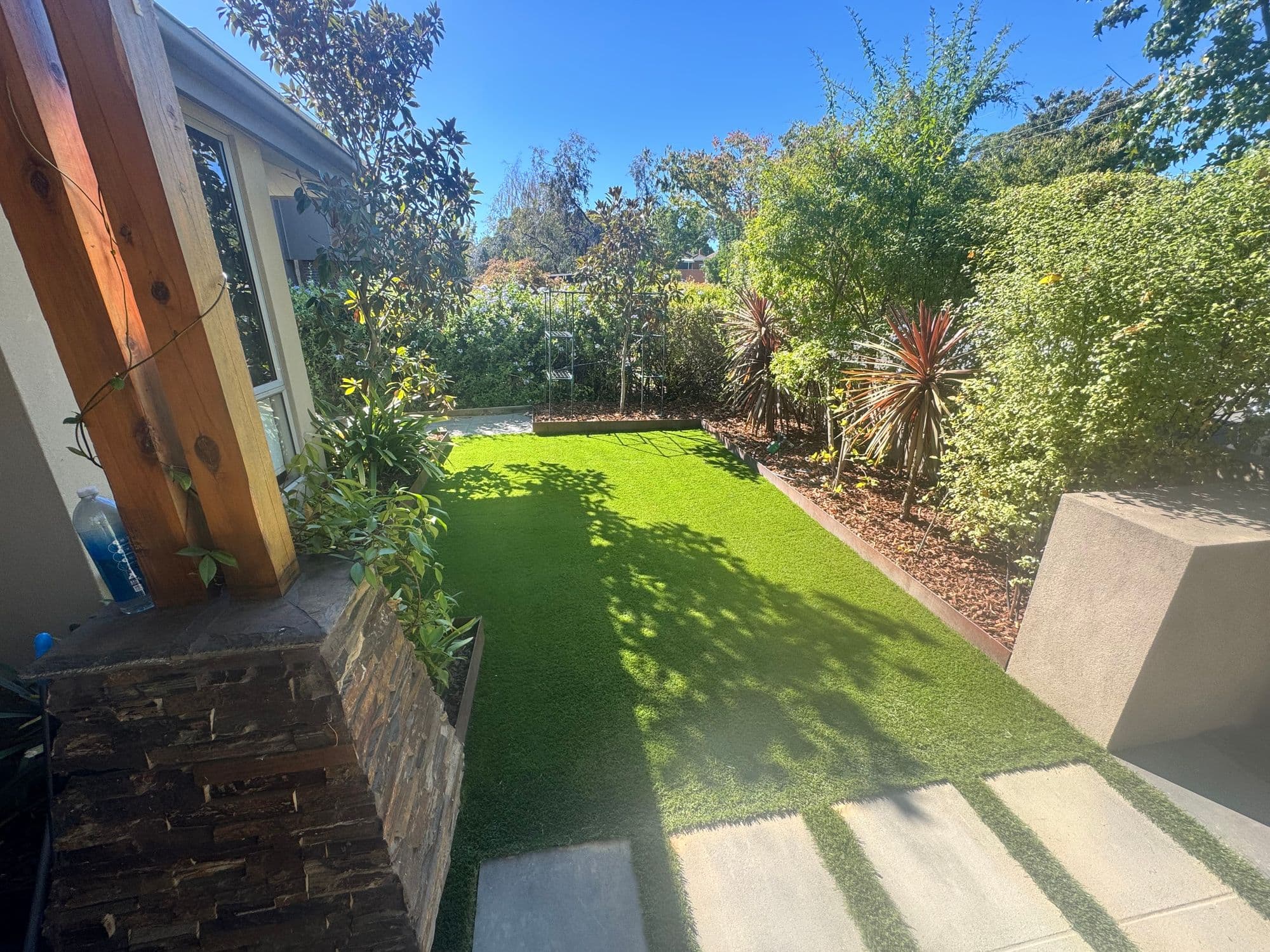 Artificial grass between concrete pavers and lush garden beds