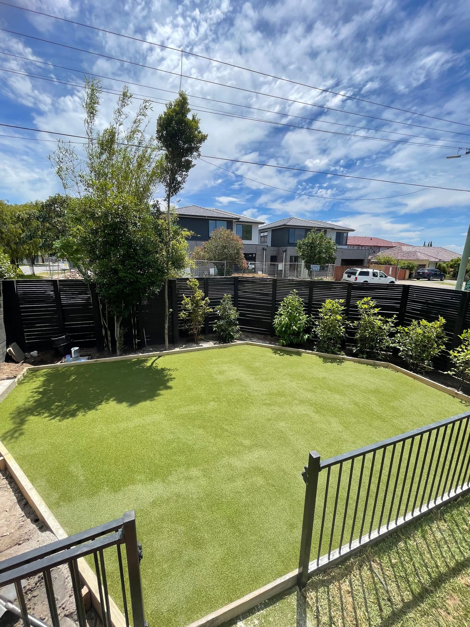 Artificial lawn inside a landscaped backyard with new screening plants and a pool fence