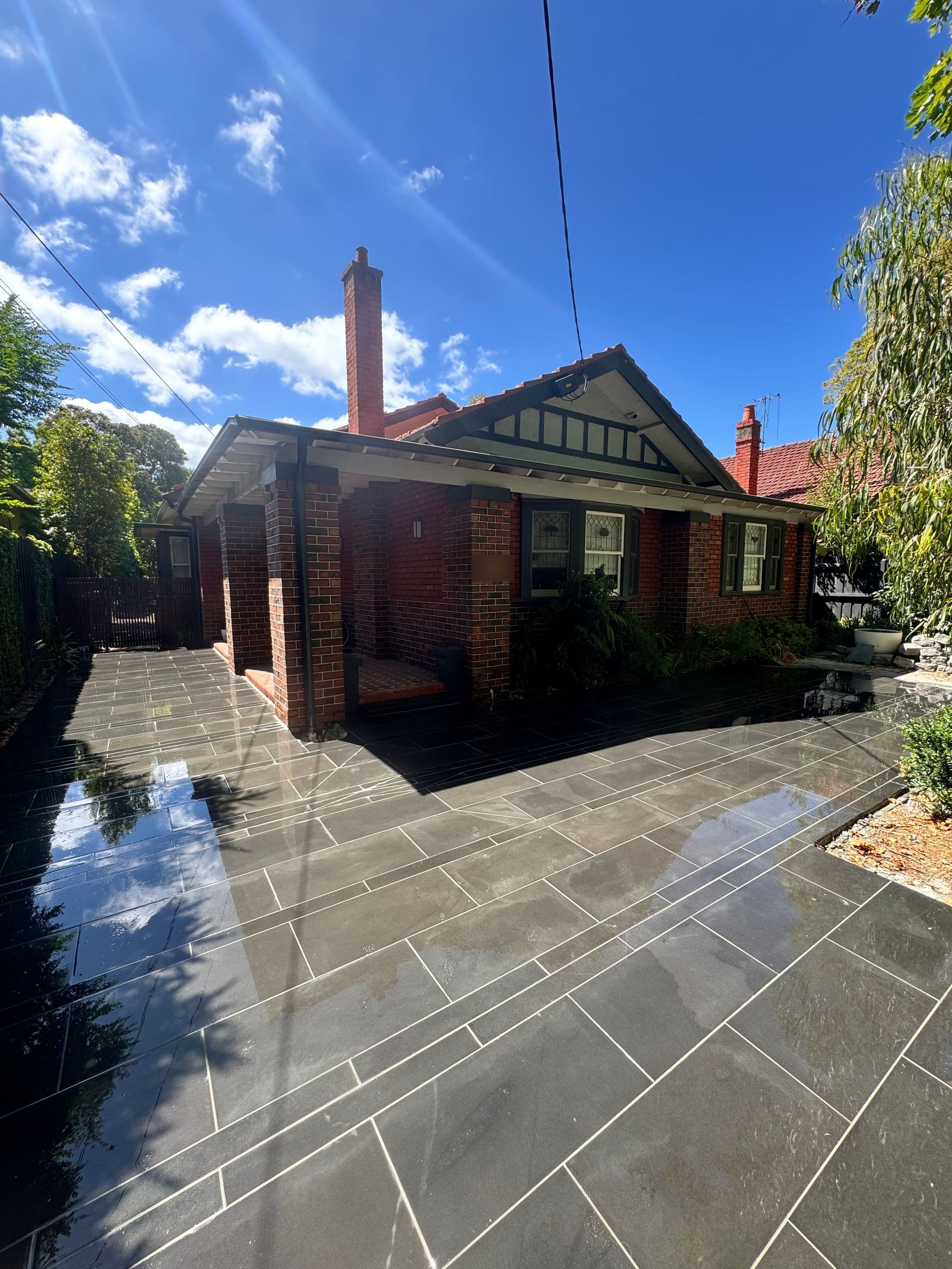 Freshly washed sawn bluestone driveway with narrow feature bands in front of a red brick bungalow