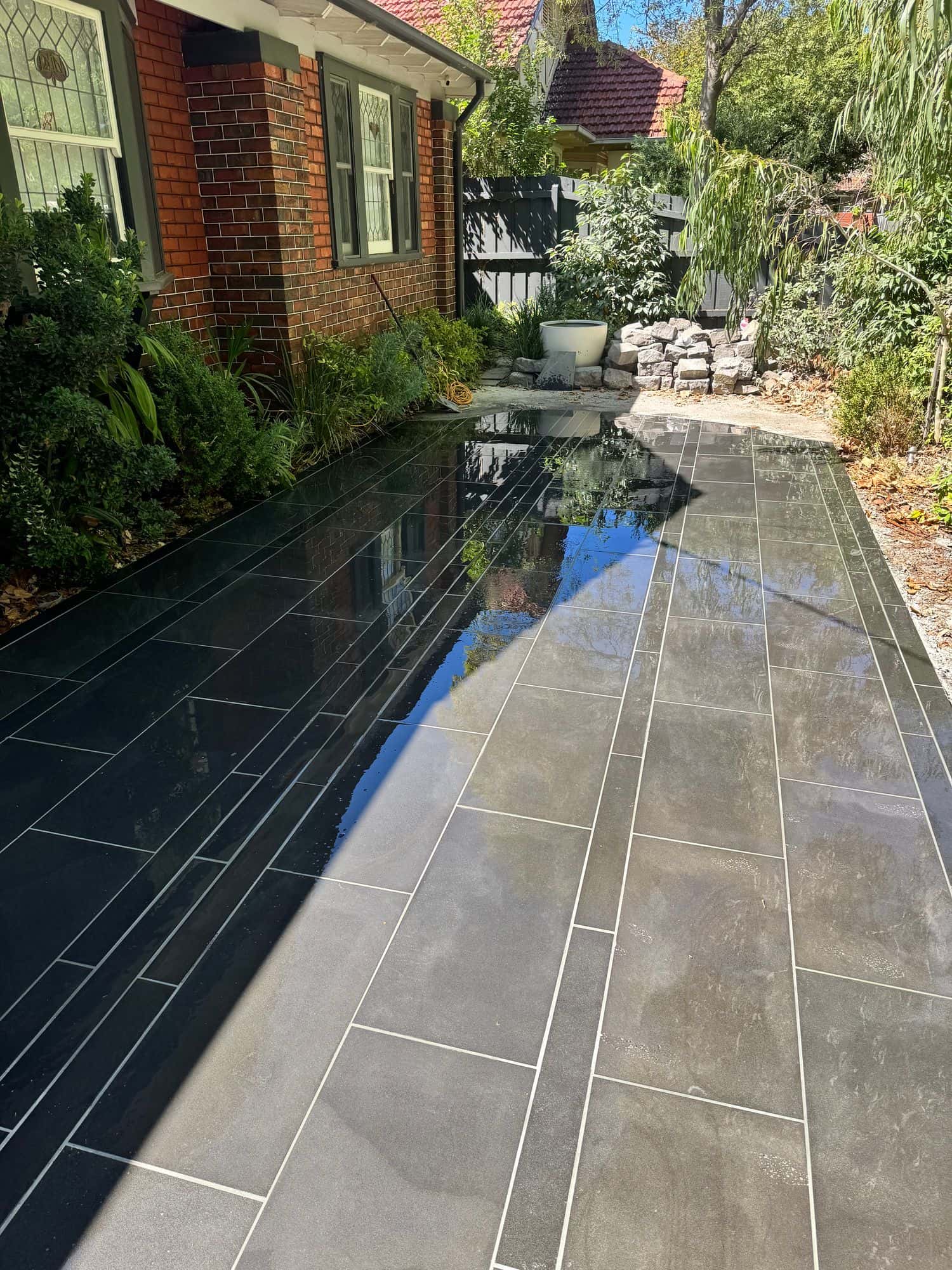 Banded sawn bluestone front path running beside a brick home and leafy garden