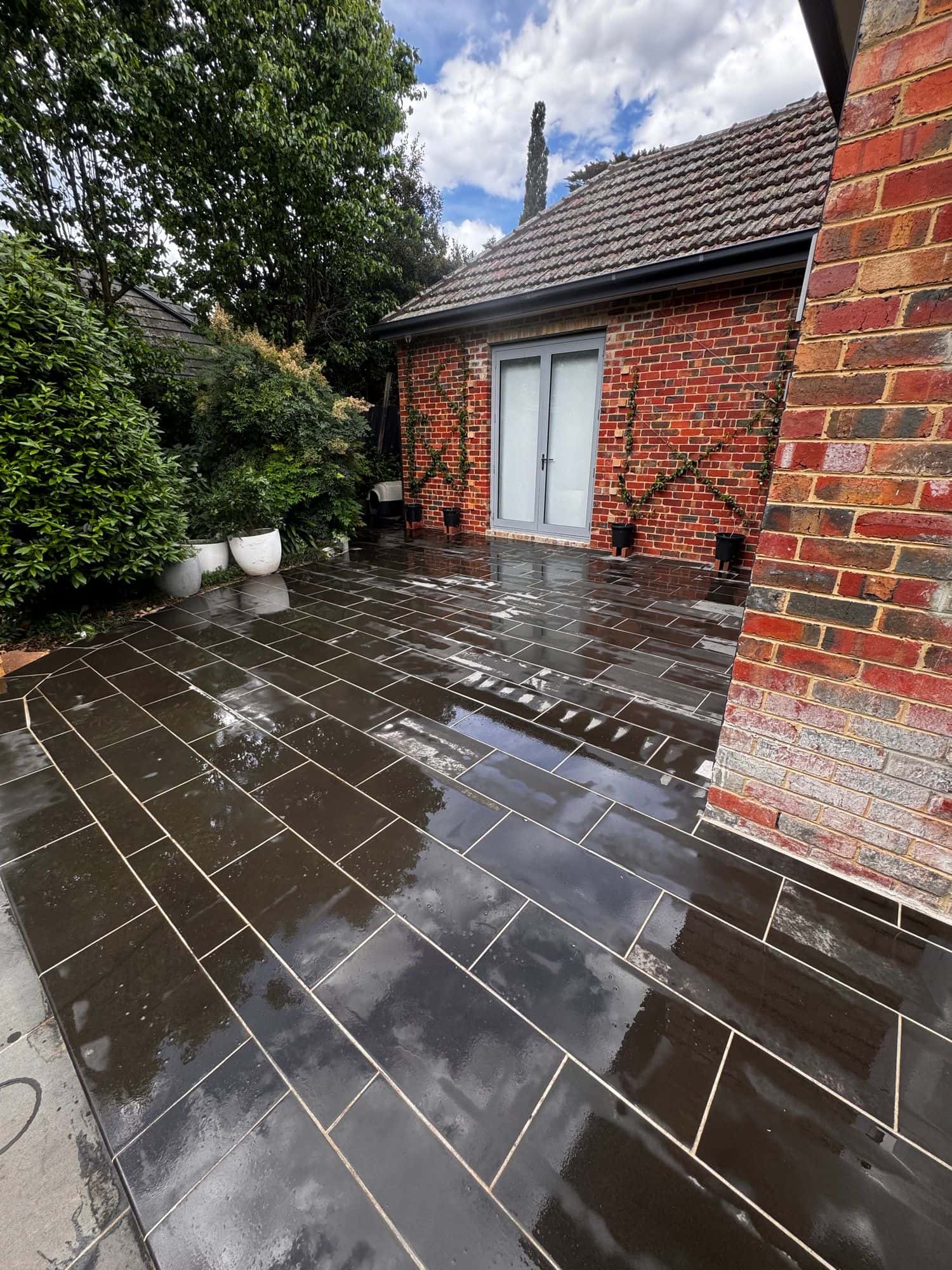 Wet sawn bluestone patio leading to French doors beside a red brick wall