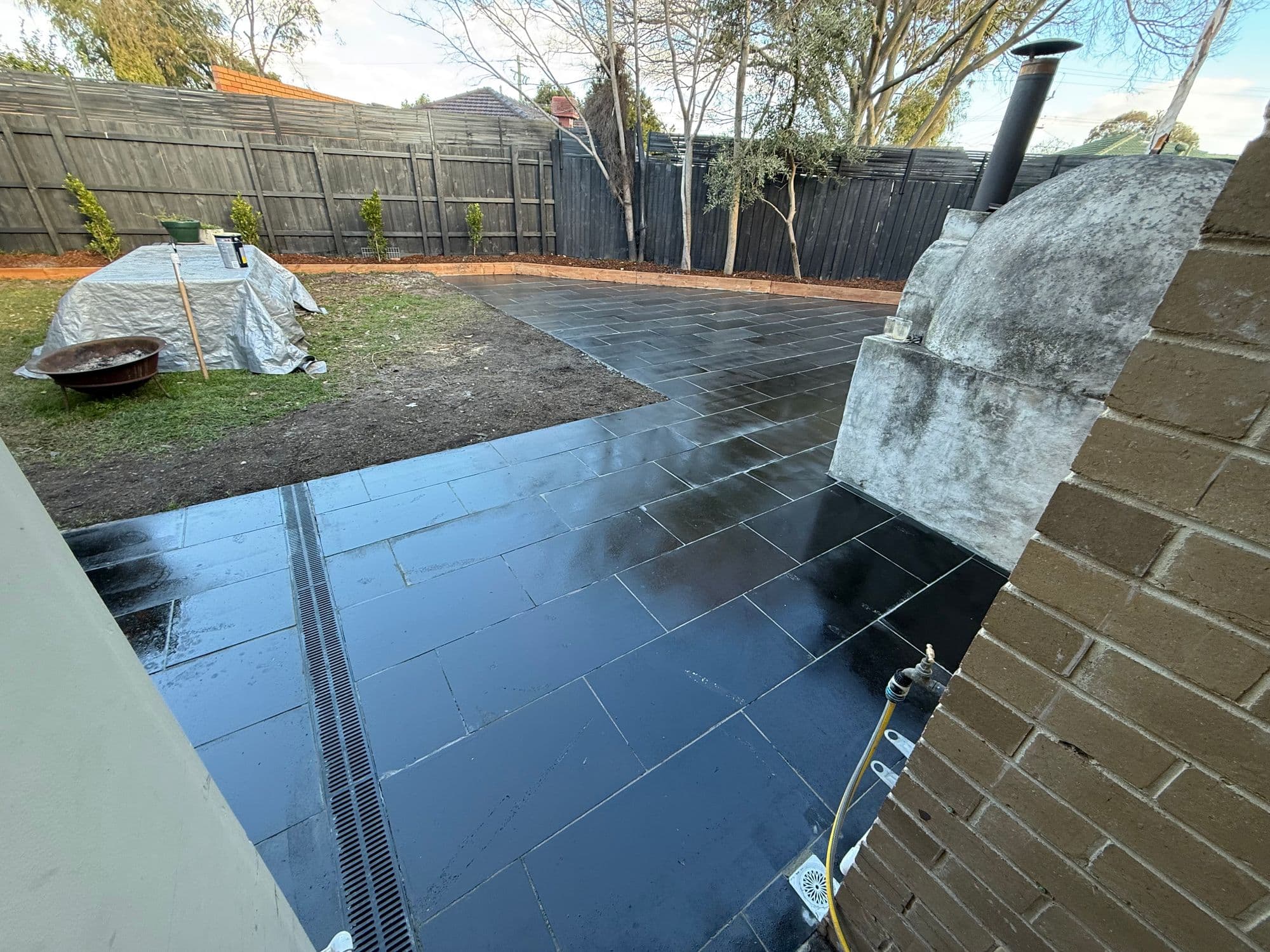 Freshly washed sawn bluestone patio with a strip drain beside a rendered pizza oven