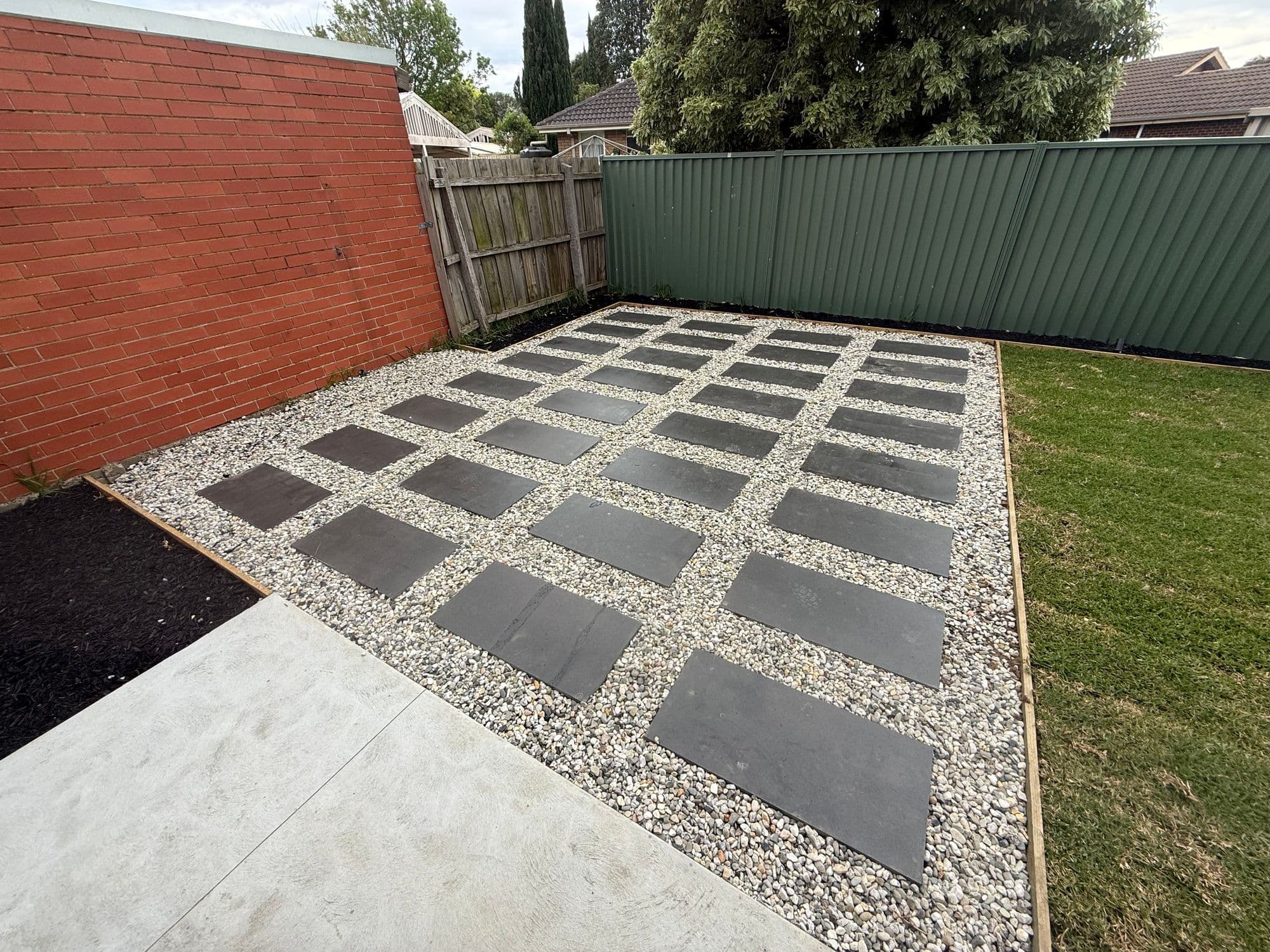A grid of large charcoal pavers set in pale pebbles beside a new lawn