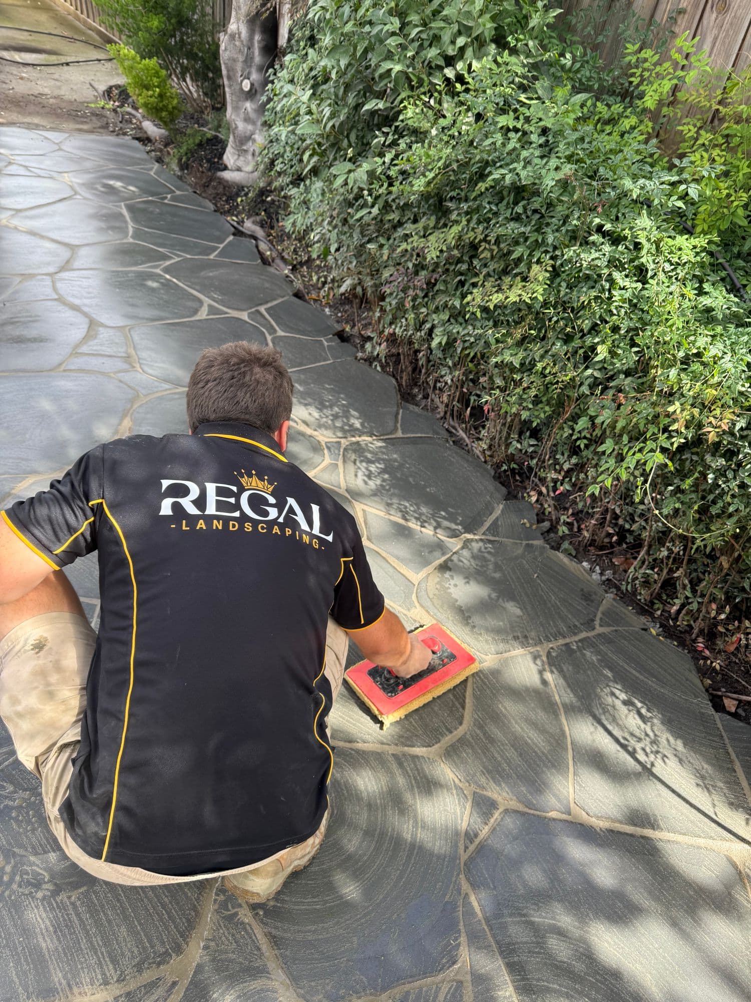 A Regal Landscaping crew member cleaning grout off newly laid bluestone crazy paving
