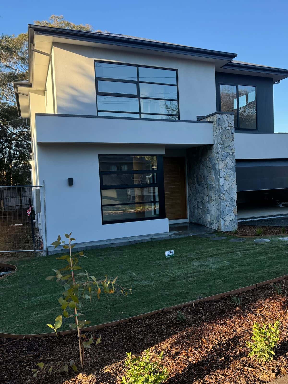 Curved Sir Walter buffalo front lawn with steel edging and freshly mulched beds at a new home