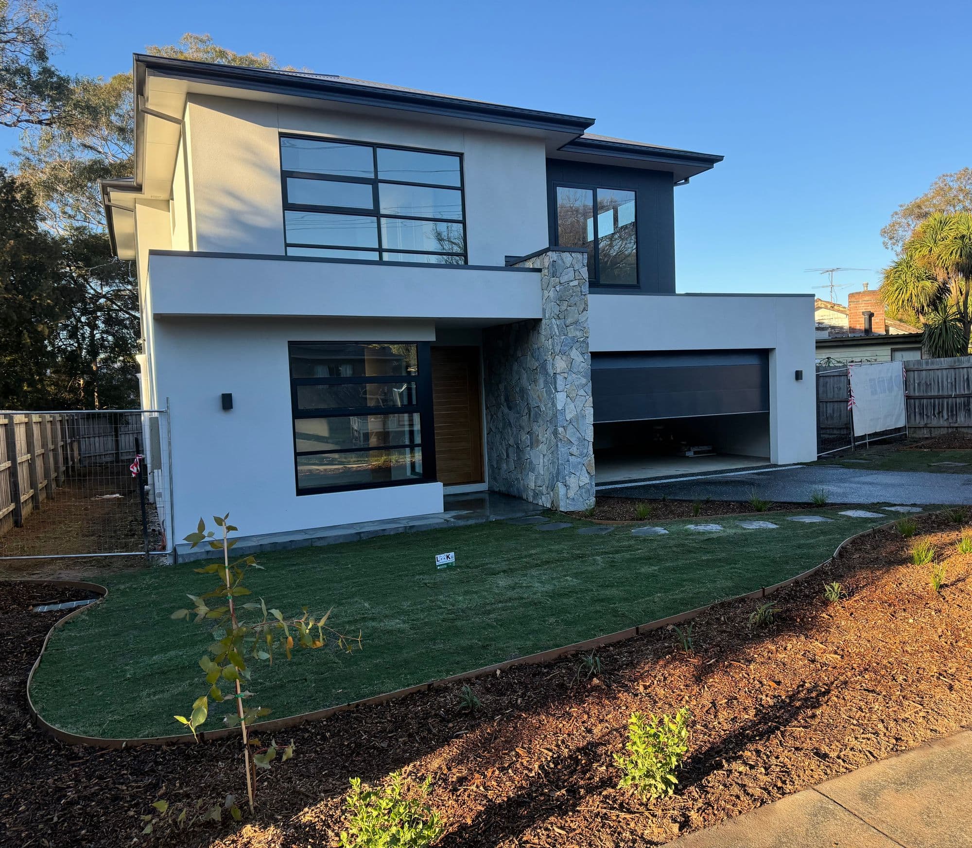 Curved Sir Walter buffalo front lawn with steel edging and freshly mulched beds at a new home