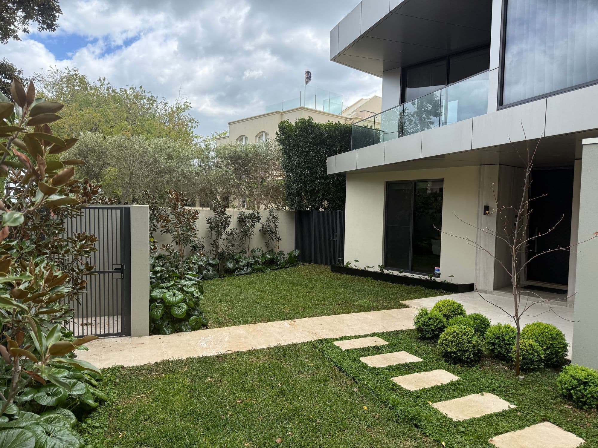 Modern front garden in Brighton with Sir Walter buffalo lawns either side of a travertine path and stepping pavers