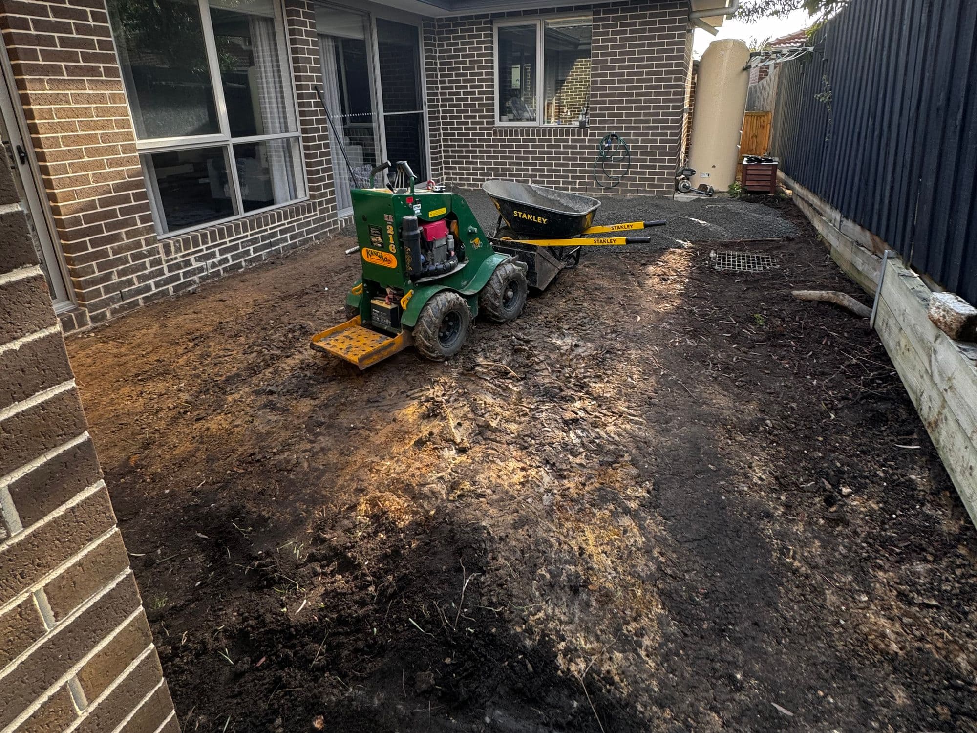 A new home's backyard stripped back to bare soil, with a mini loader ready to level it