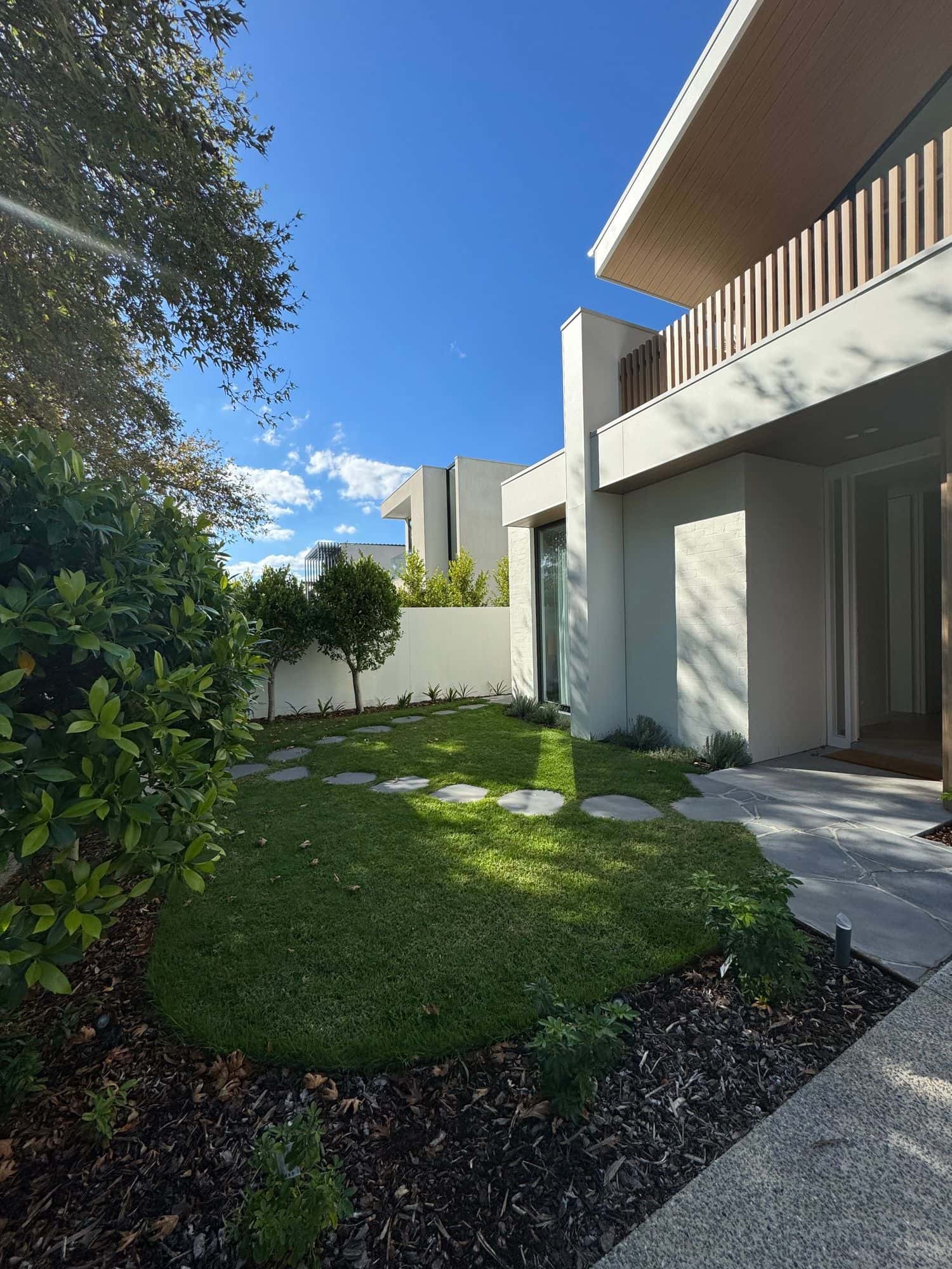 An arc of stepping stones across a new lawn to the crazy-paved entry of a modern home