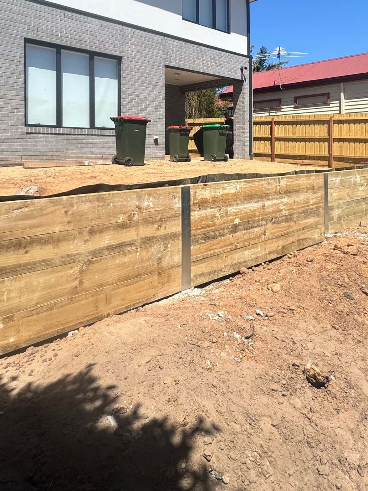 Large timber sleeper retaining wall with galvanised steel posts beside a new two-storey home