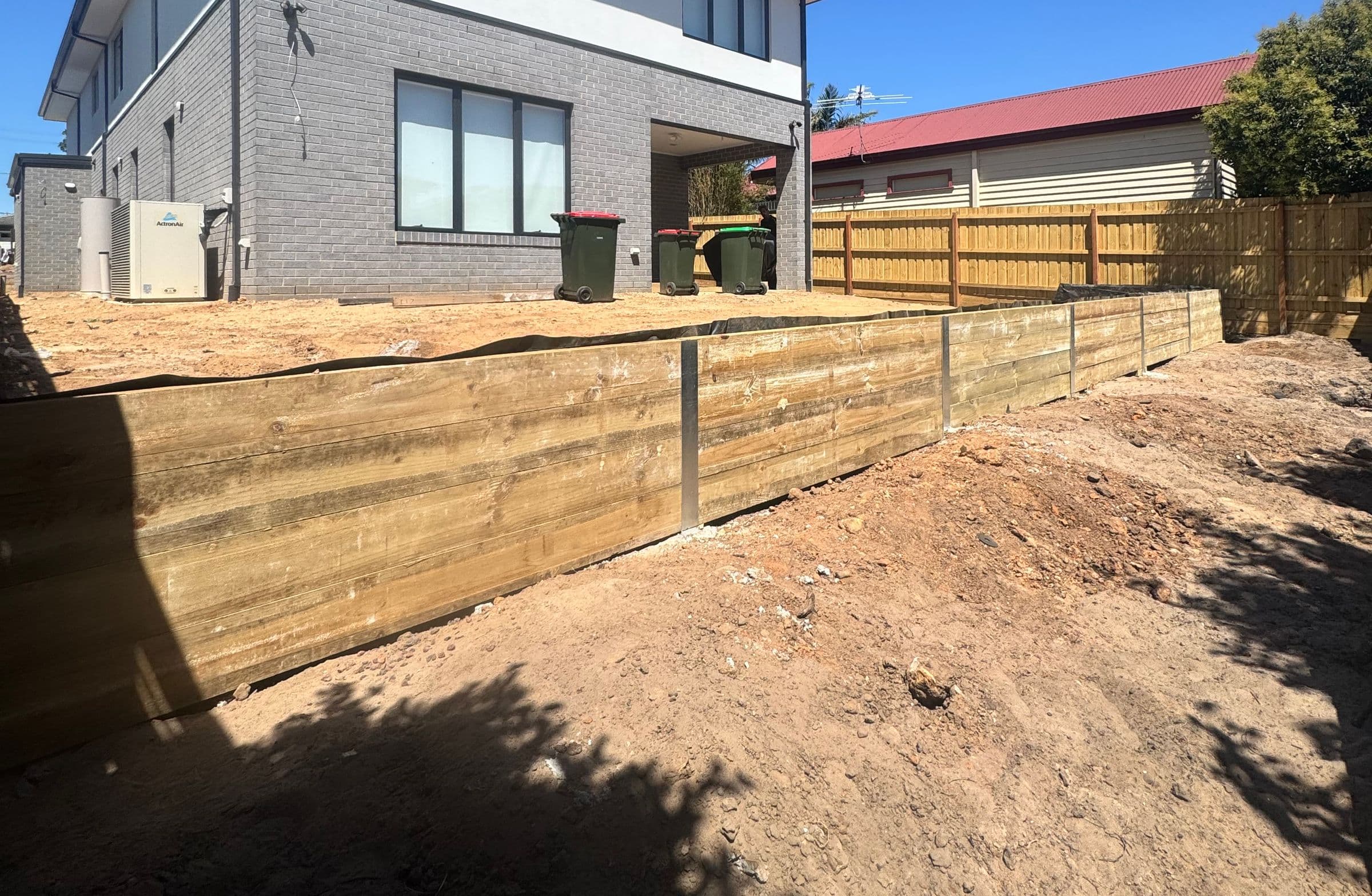 Large timber sleeper retaining wall with galvanised steel posts beside a new two-storey home